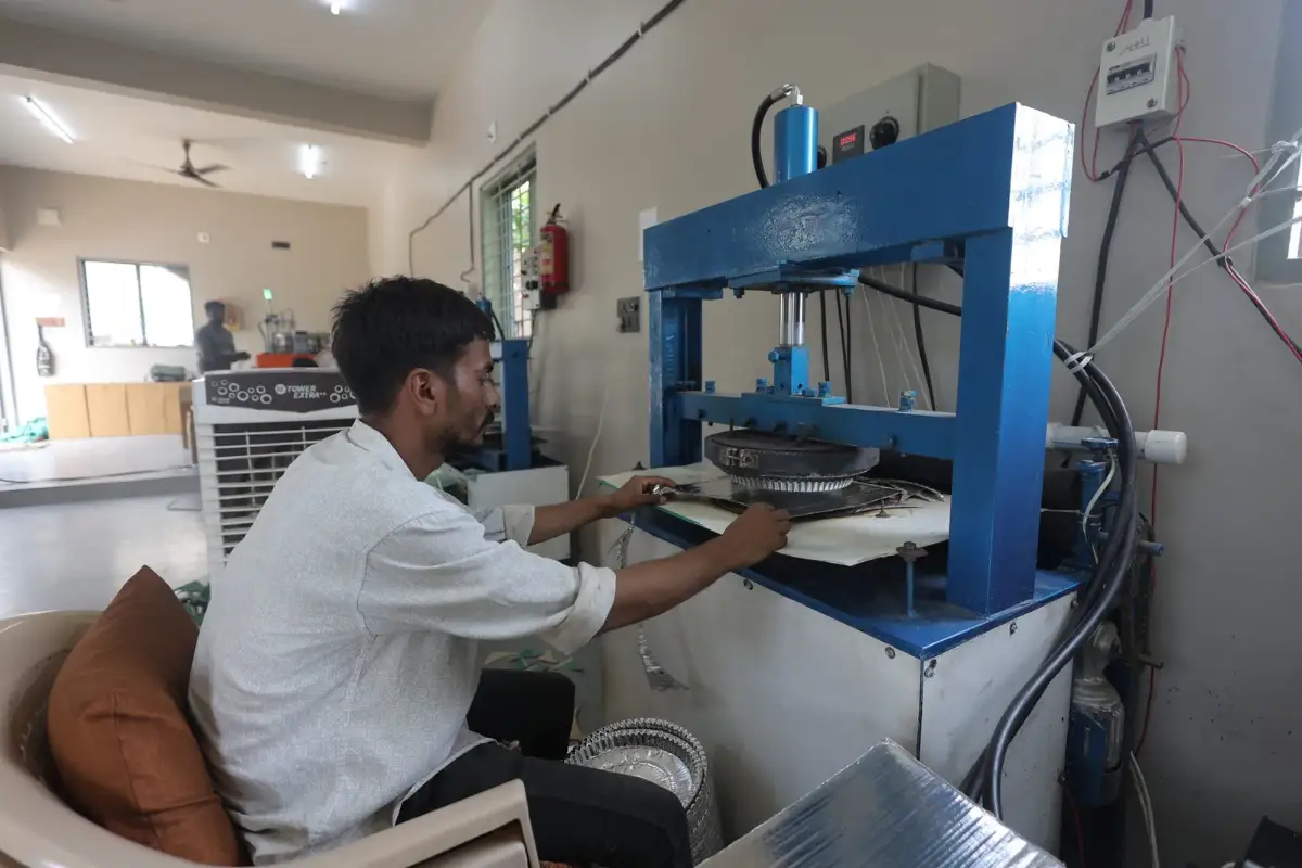 Worker pressing a silver paper dish on the hydraulic press